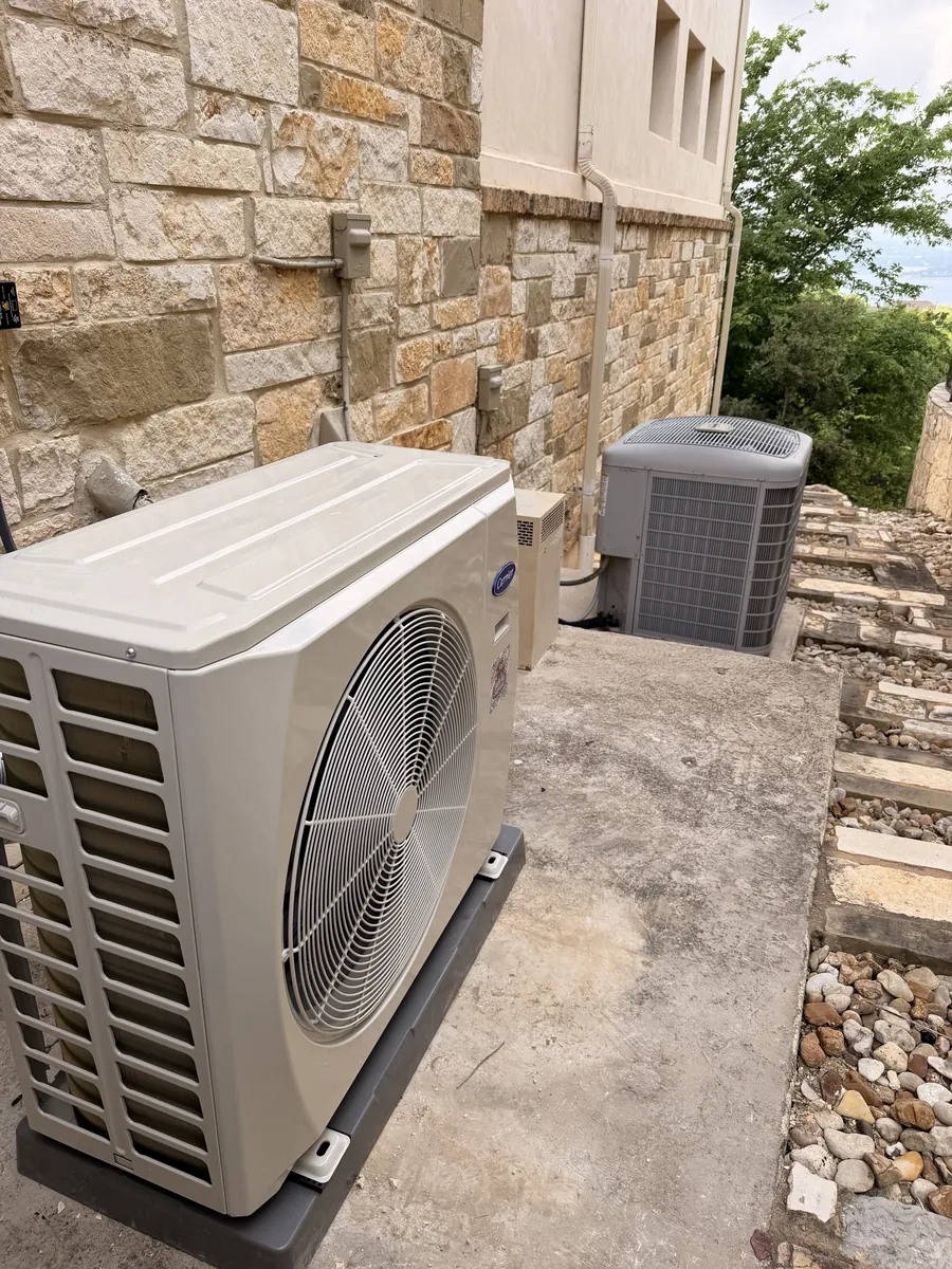 Carrier outdoor condenser unit installed against stone home siding in Leander, Texas